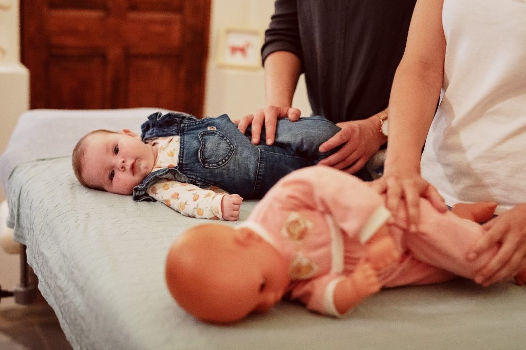 De ouder leert van de kinderfysiotherapeut de oefeningen die zij dagelijks kan uitvoeren om de motoriek te stimuleren van de baby. 